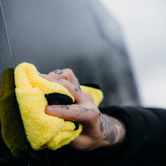Person cleaning a car with a yellow microfiber cloth