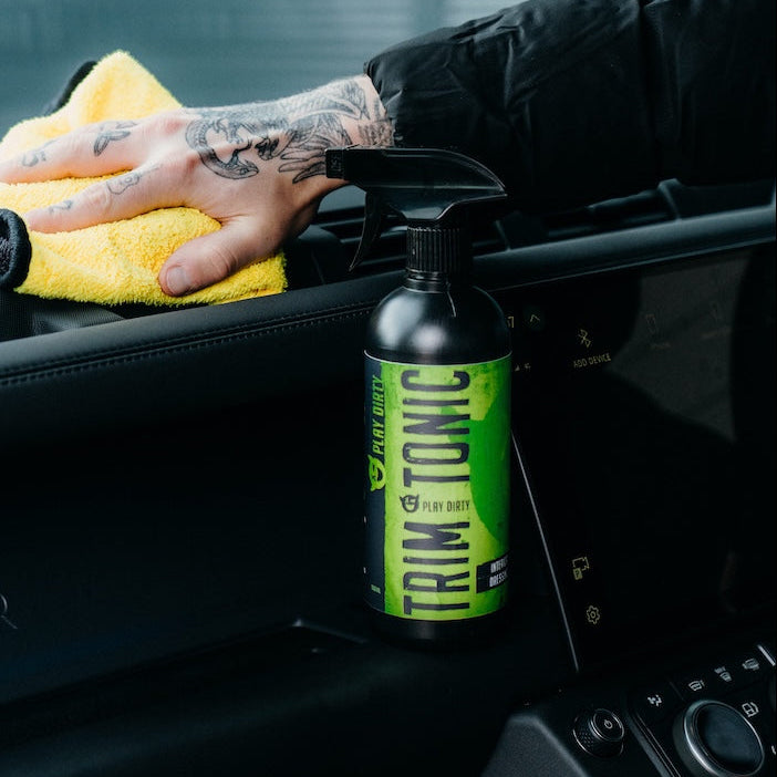 Person cleaning car interior with a spray bottle and yellow cloth