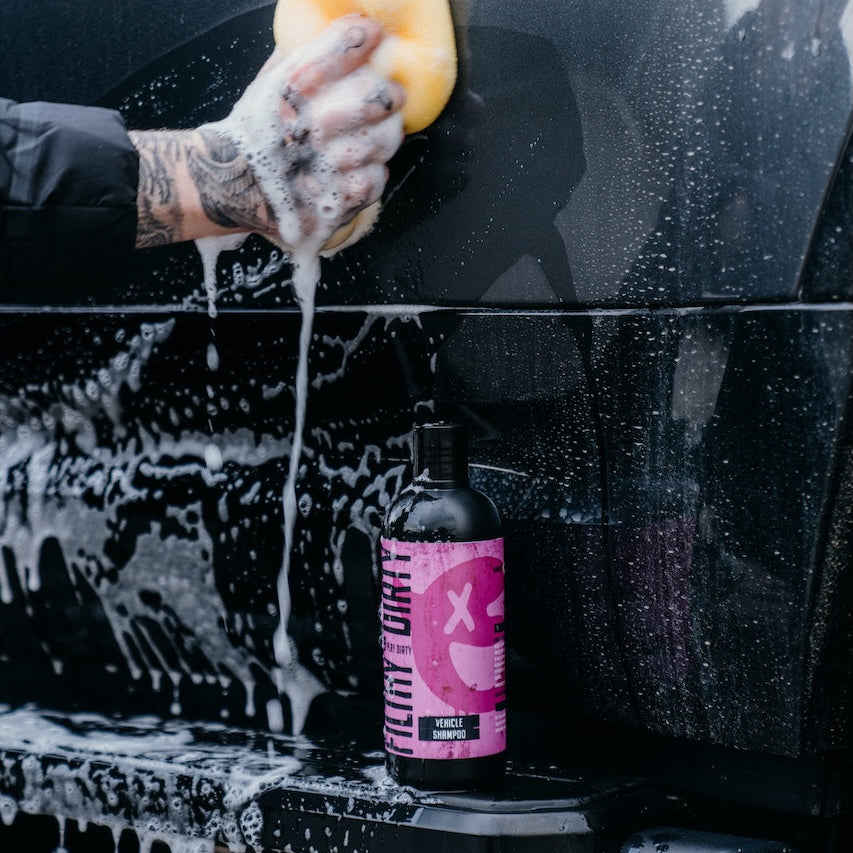 Person washing a car with a sponge and a bottle of car wash product on a black car.